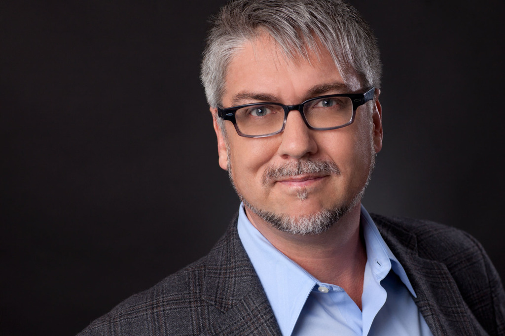 Go-To expression headshot of smiling man on black background. Glasses. Beard.