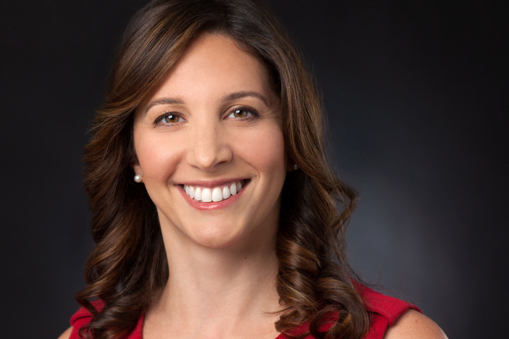 Professional Headshot of Smiling Brunette Woman in red dress on black background. 