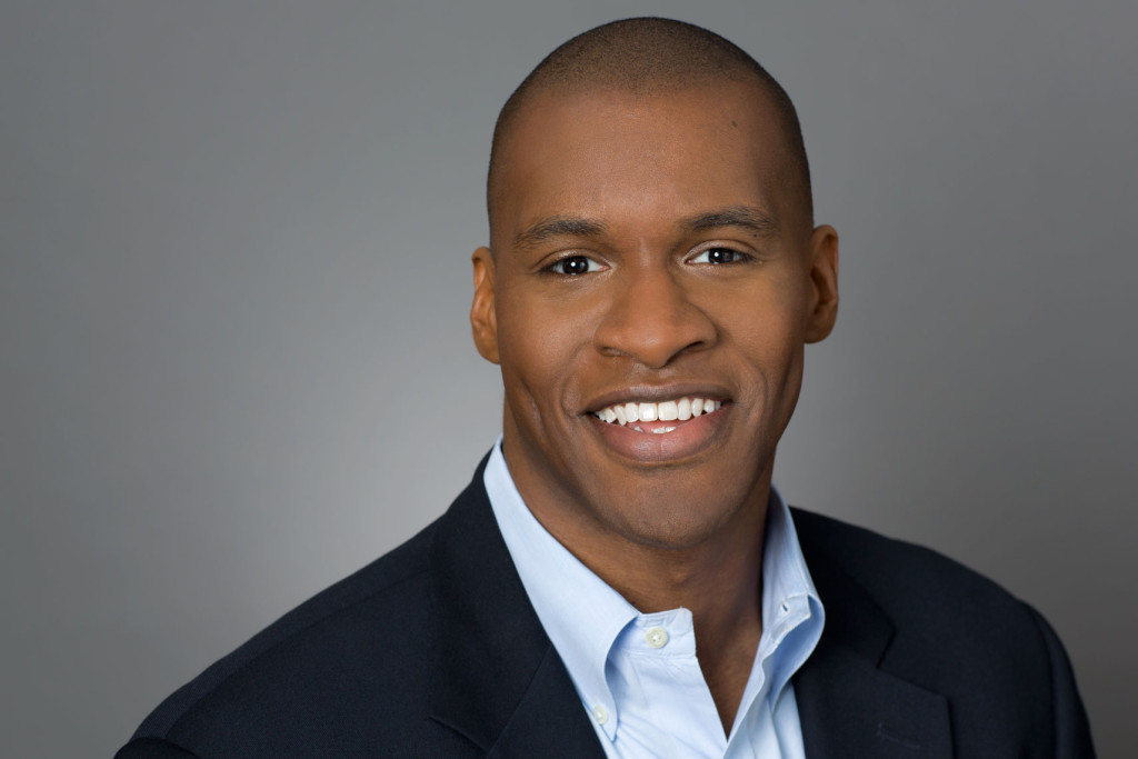 Company Headshot of man in blazer on a grey background. 