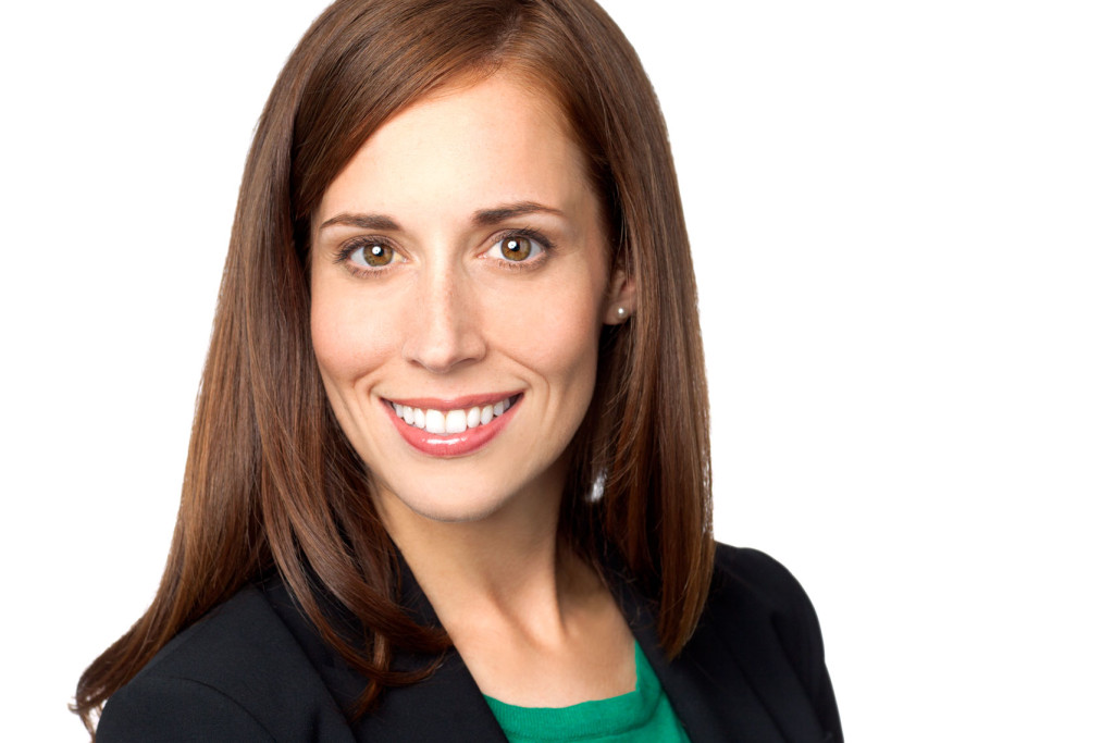 Headshot of smiling woman in black suit and green blouse on white background.