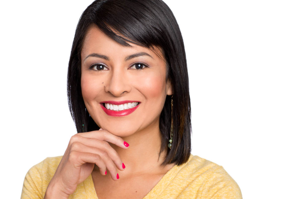 Woman in yellow sweater uses her hand in this headshot on a white background.