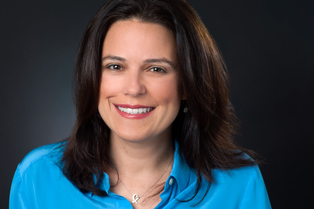 Headshot of Author Tracy Sestili in blue shirt on black background.